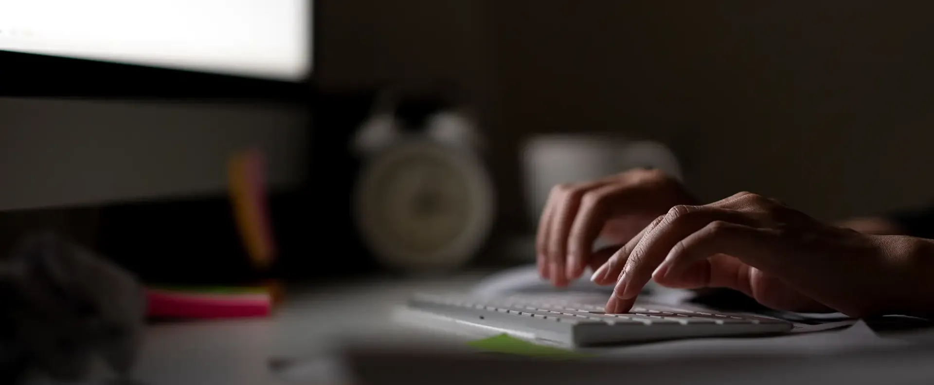 Hands typing on a computer keyboard while working online in a dark office.