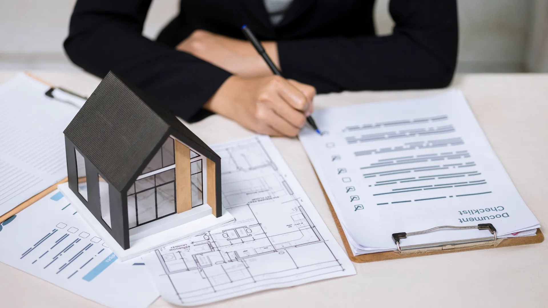 Model home on architectural plans beside a person reviewing financing documents
