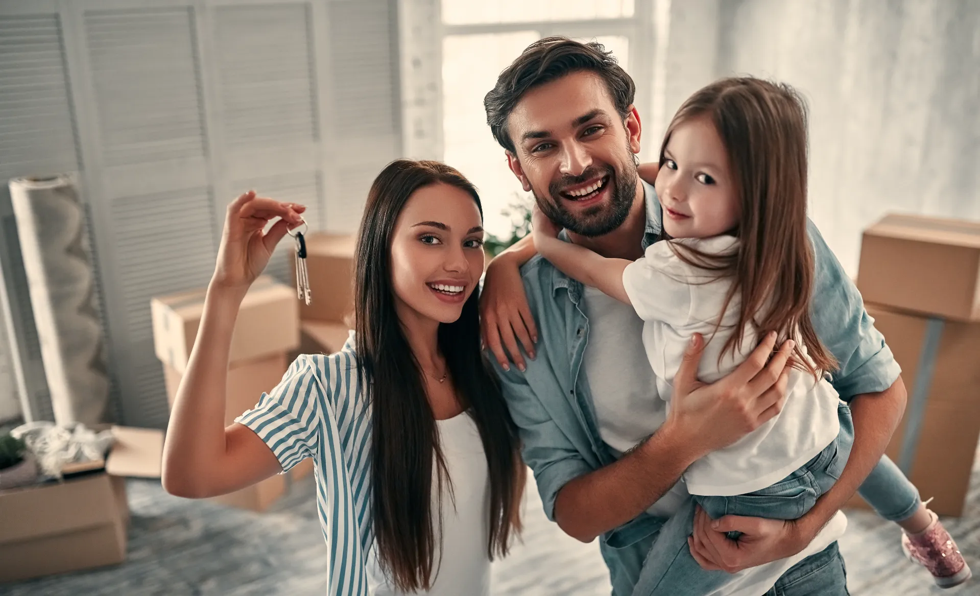 Family holding the keys to their new home while unpacking moving boxes